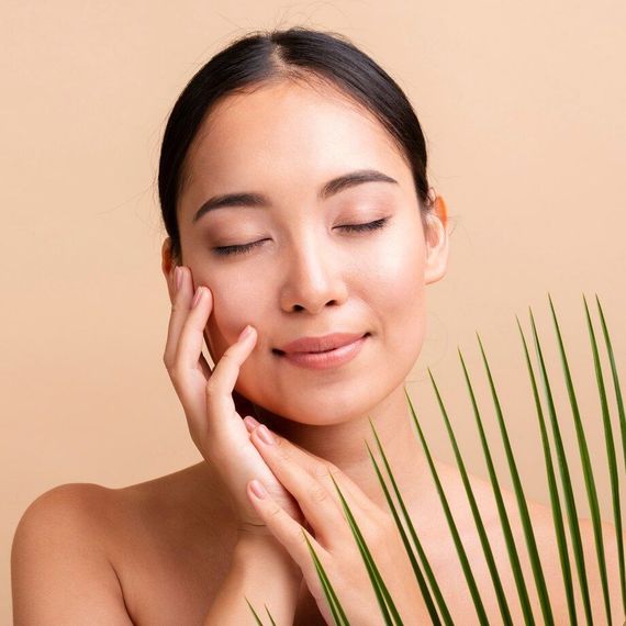 A woman is touching her face with her hands and holding a palm leaf.