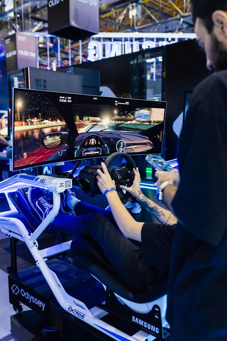 Person racing in a driving simulator at a gaming expo, with blue-lit cockpit and large display screens