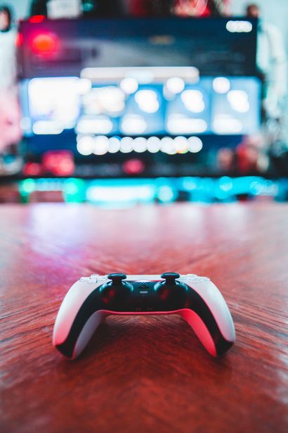 White game controller on a wooden table, with a blurred TV screen glowing in the background.