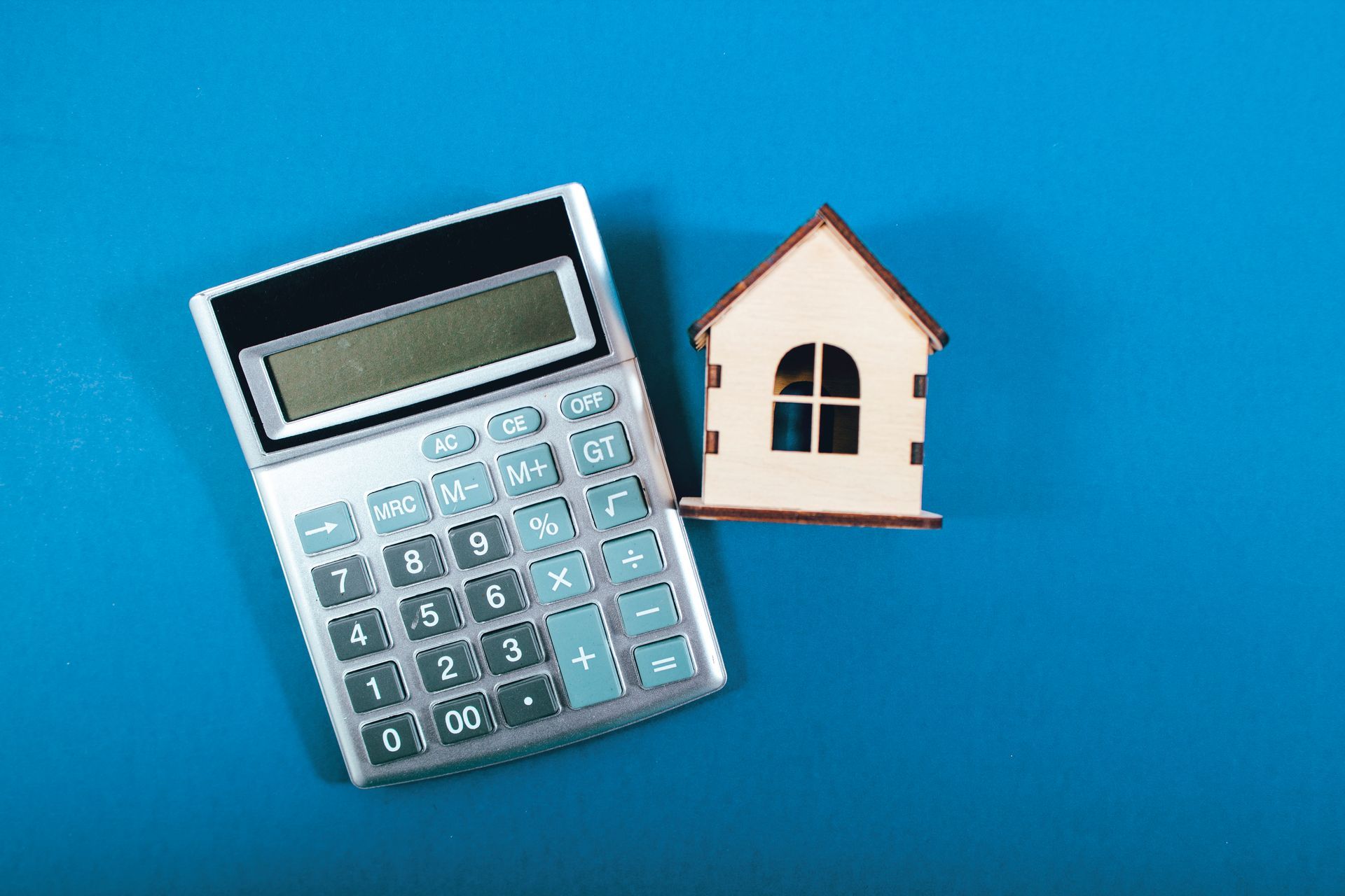 Calculator and small wooden house on a blue surface, representing home finances.