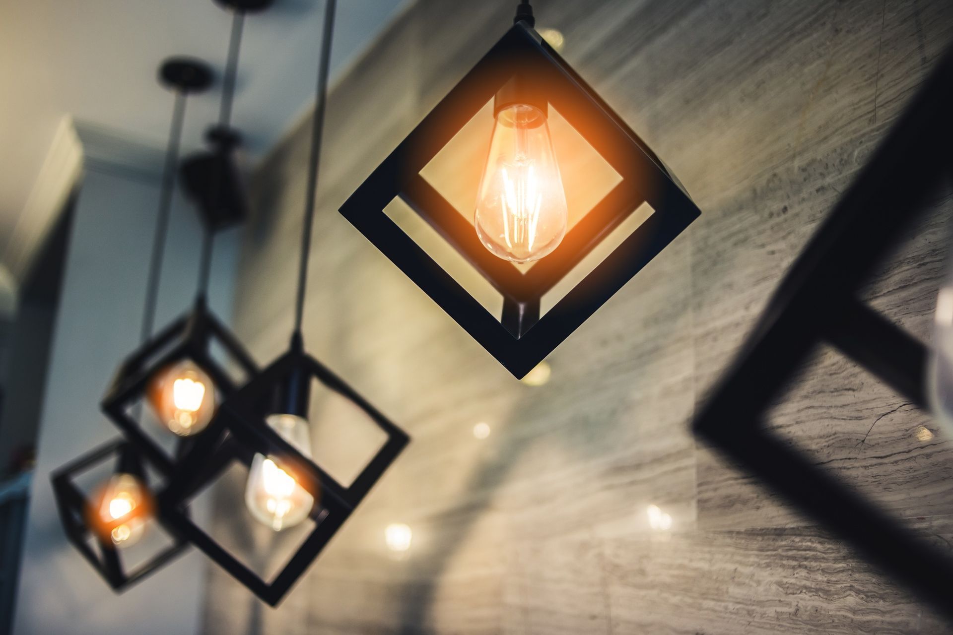 Hanging black metal pendant lights with warm glowing bulbs against a textured wall