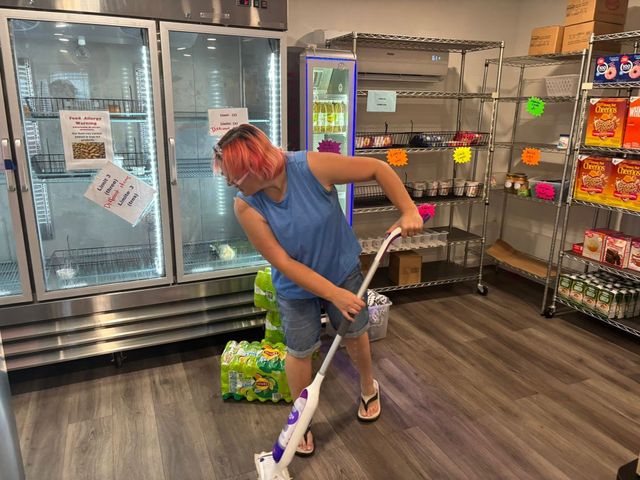 Person mopping a store floor near refrigerated cases and snack shelves.
