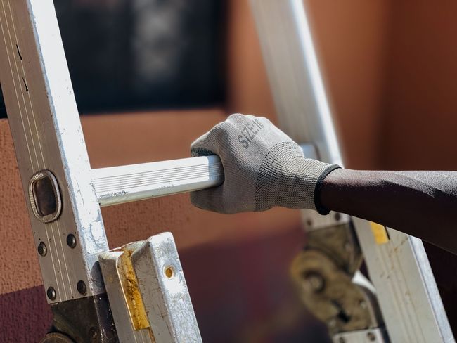 Gloved hand holding a silver tool against a metal ladder rung indoors