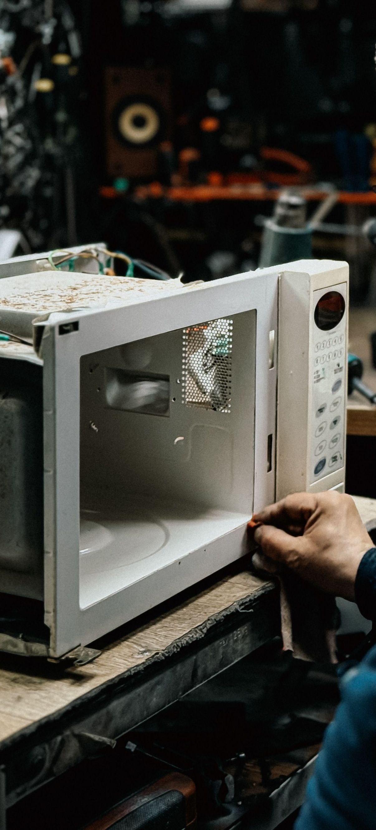 White microwave on a workbench with its door open, showing a person’s hand repairing it in a workshop
