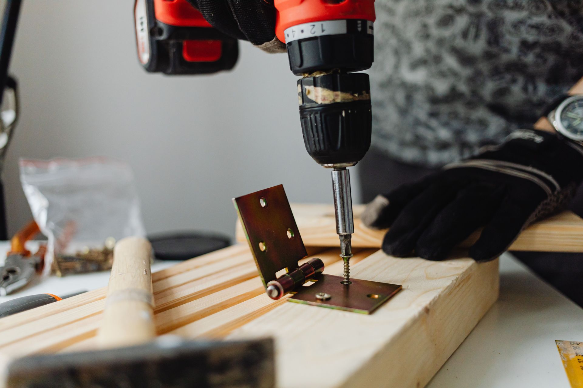 Cordless drill fastening a metal hinge on a wooden board during a DIY project