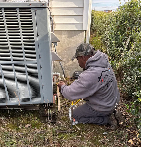 Technician kneeling beside an outdoor HVAC unit, checking connections with tools near a house.