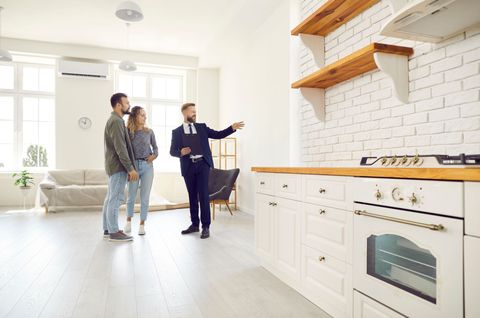 Two people and a realtor in a bright white kitchen, discussing the open shelving and stove
