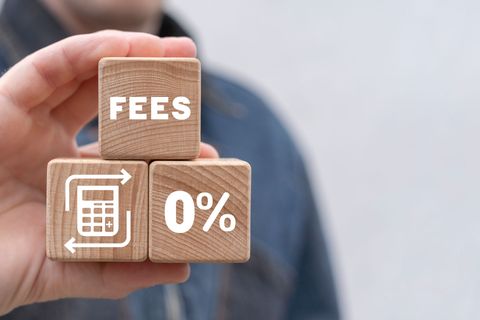 Hand holding wooden blocks labeled “FEES” and “0%” with a calculator icon on a blurred background
