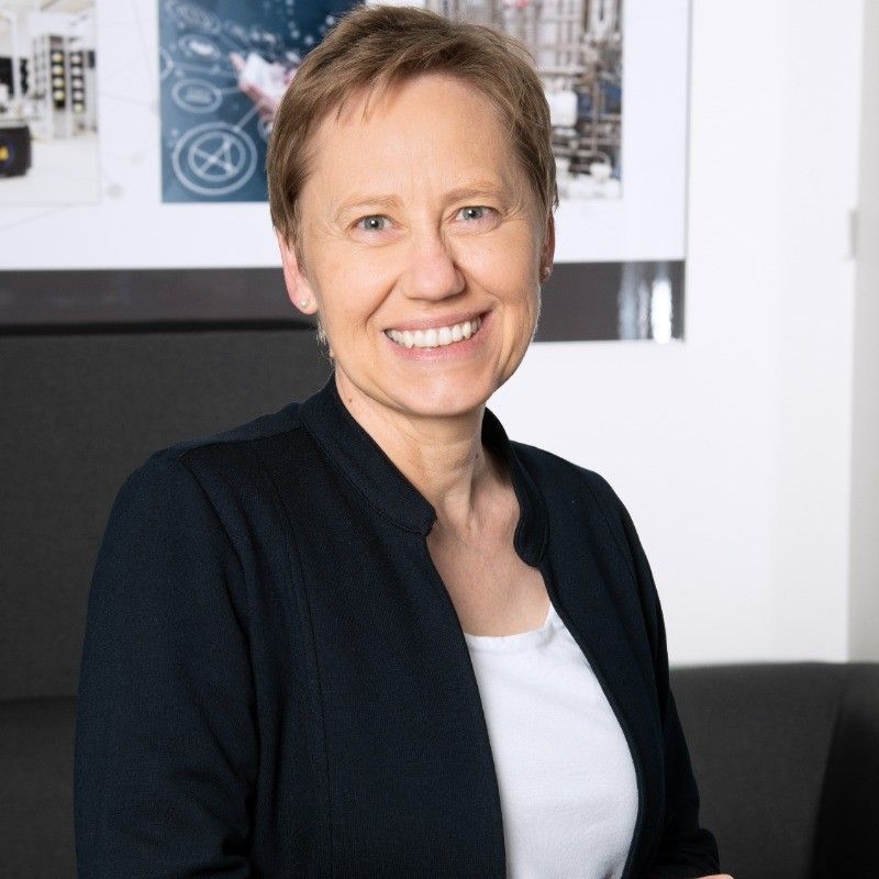 Eine Frau in einer schwarzen Jacke und einem weißen Shirt lächelt in die Kamera.