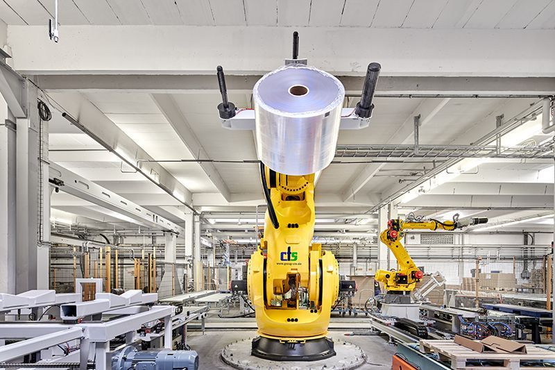 In einer Fabrik hält ein Roboterarm eine Rolle Plastikfolie.