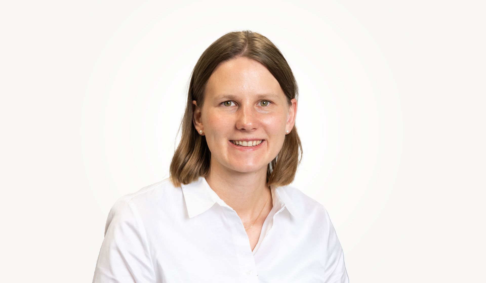 Eine Frau in einer weißen Bluse lächelt in die Kamera.