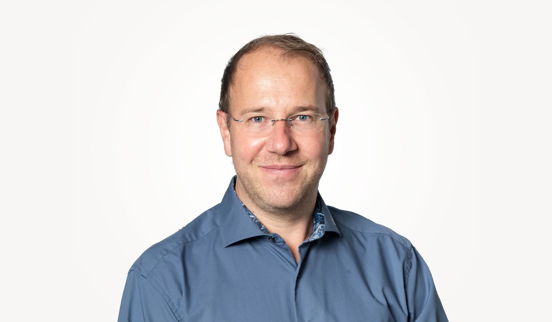 Ein Mann mit Brille und blauem Hemd lächelt in die Kamera.