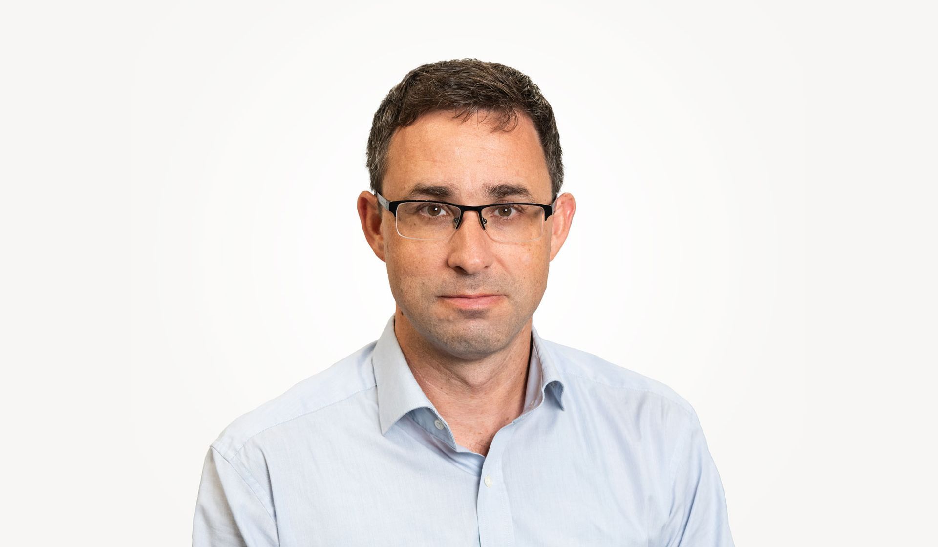 Ein Mann mit Brille und hellblauem Hemd schaut in die Kamera.
