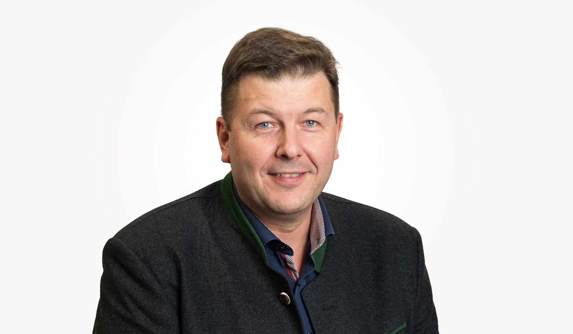 Mitarbeiter der cts in traditioneller dunkler Jacke, lächelnd, neutraler Hintergrund.