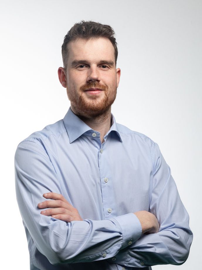 David Laimer, Geschäftsführer Adopt SMT Group Man with crossed arms, light blue shirt, and a beard, smiling against a white backdrop.