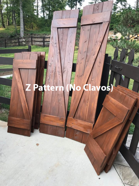 Wooden Z-pattern fence panels leaning outdoors on a concrete patio with trees in the background