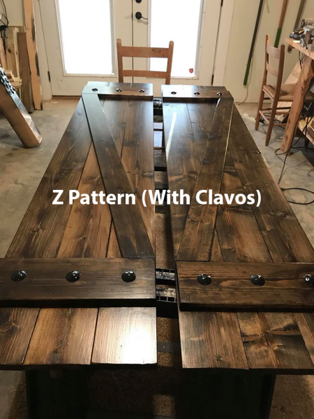 Wooden Z-pattern barn door with black Clavos hardware, shown indoors on a work table