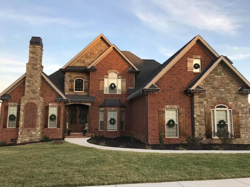 Brick suburban house with multiple gables, chimney, and a front lawn under a clear sky