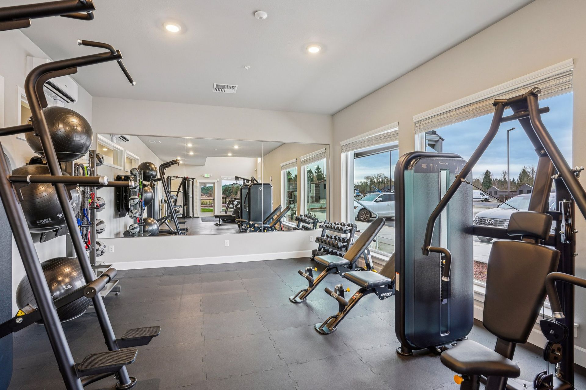 Modern home gym with exercise machines, mirrors, and large windows overlooking a neighborhood.