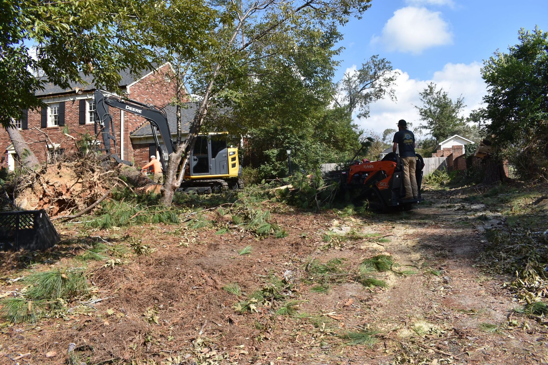 A man is standing next to a bulldozer in a dirt field in front of a house.