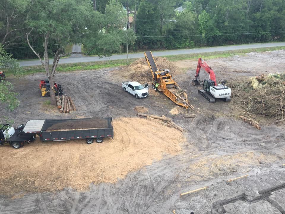 An aerial view shows heavy machinery, a pickup truck, and a dump trailer at a dirt construction or land clearing site.