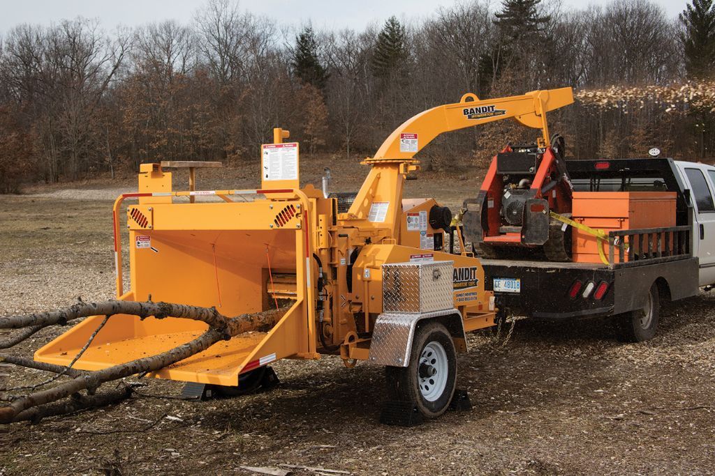 Wood chipper breaking down large limbs on job site, worked on by Top'em & Drop'em in Longwood, FL.