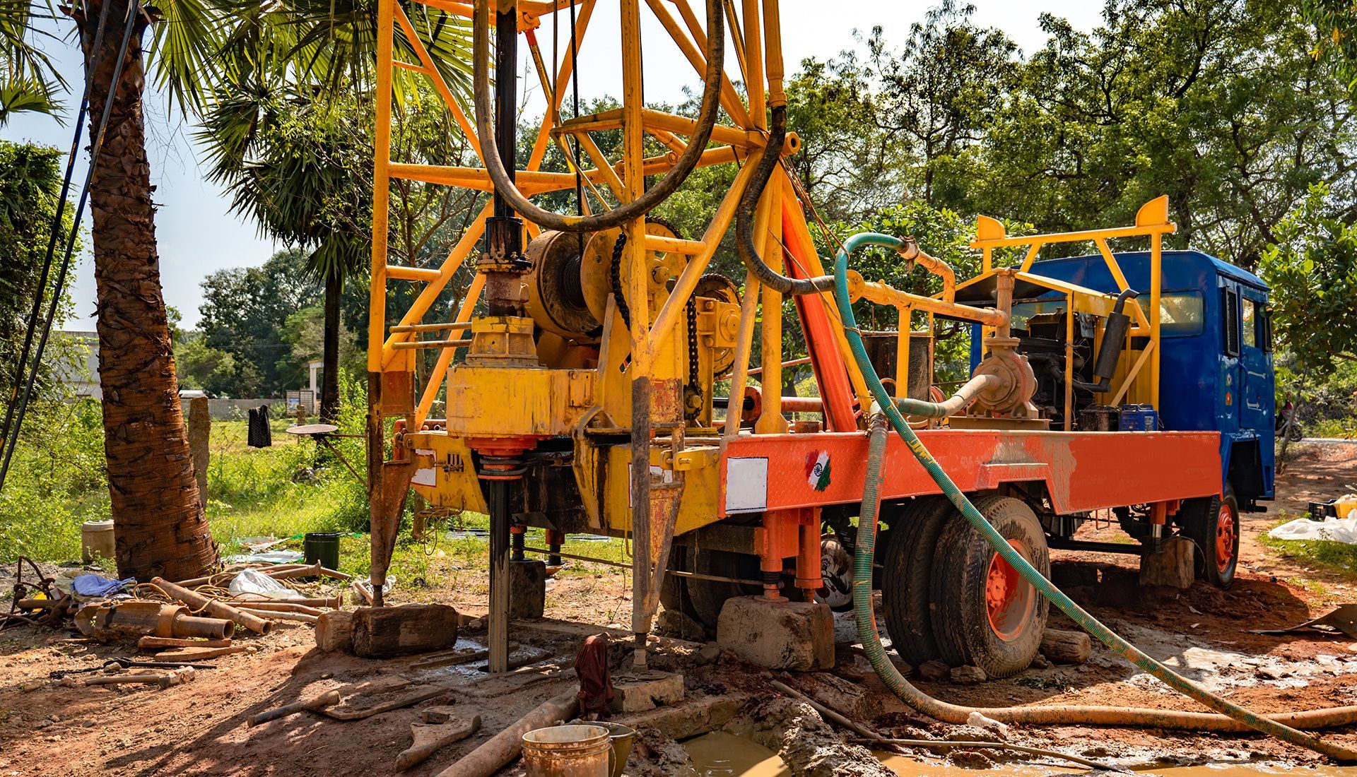 Yellow drilling rig on a truck, in a muddy field, likely for well digging.