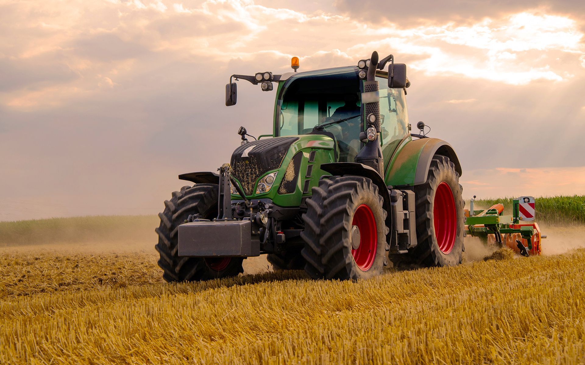 Green tractor plowing a field under a cloudy sky.