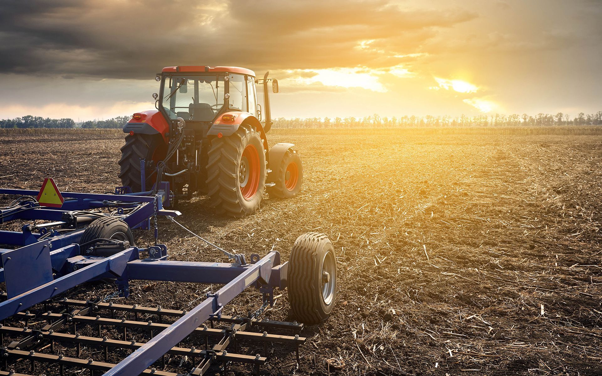 Red tractor plowing a field at sunset.