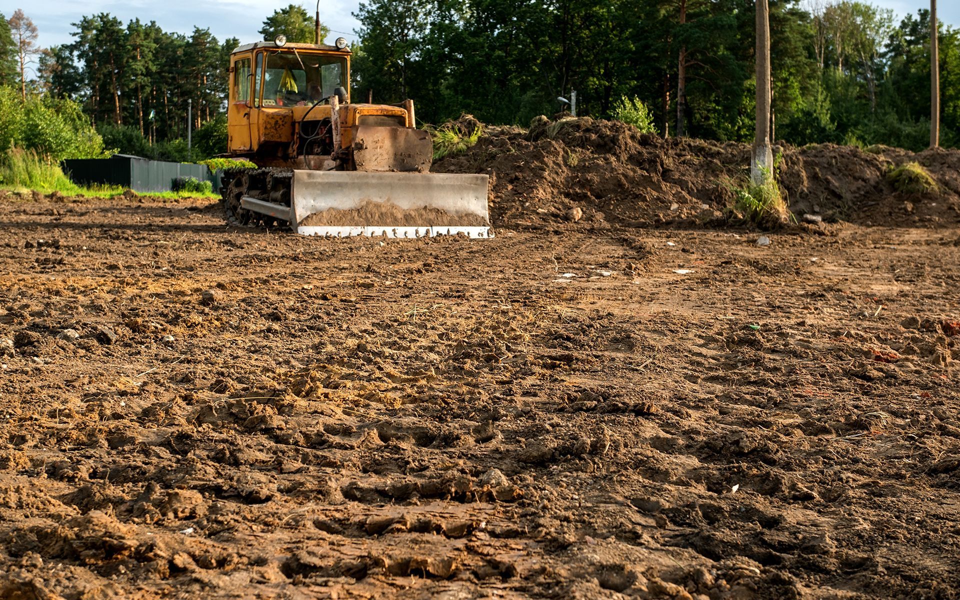 Bulldozer flattening muddy ground at construction site.
