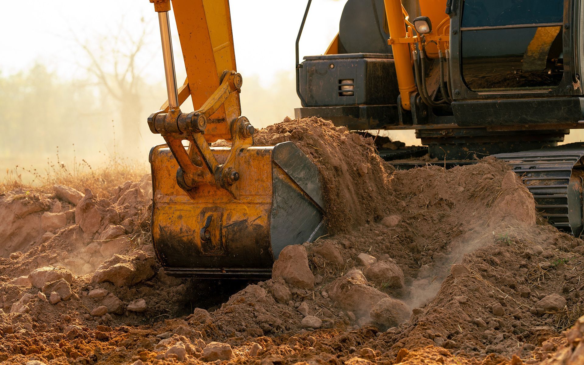 Yellow excavator scooping up brown soil in a field; construction work.