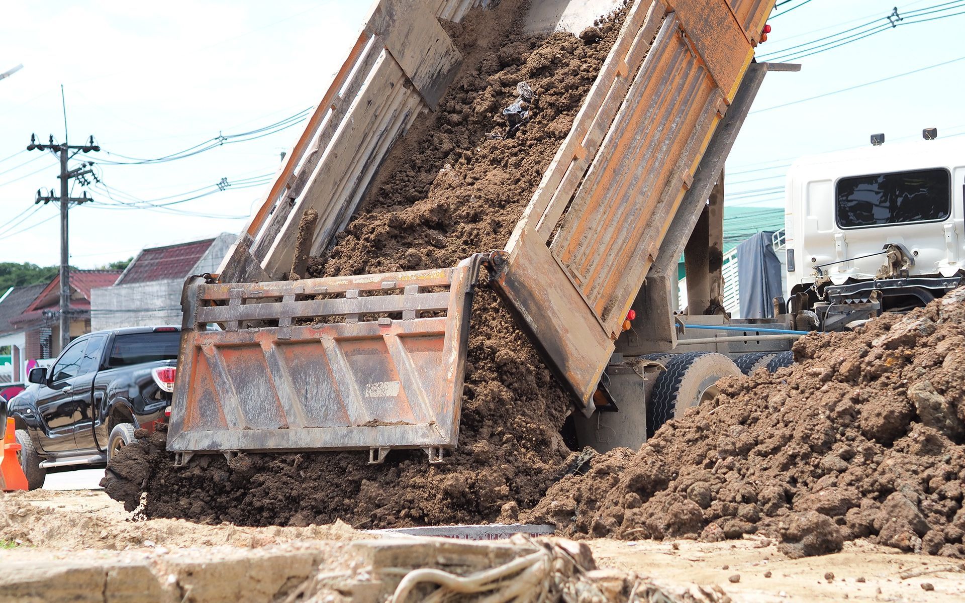 Dump truck unloading dirt onto a construction site, orange truck bed tilted, cloudy day.