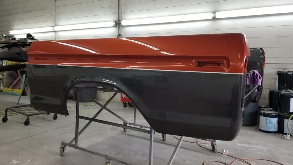 Two-toned pickup truck bed, orange and gray, in a workshop.