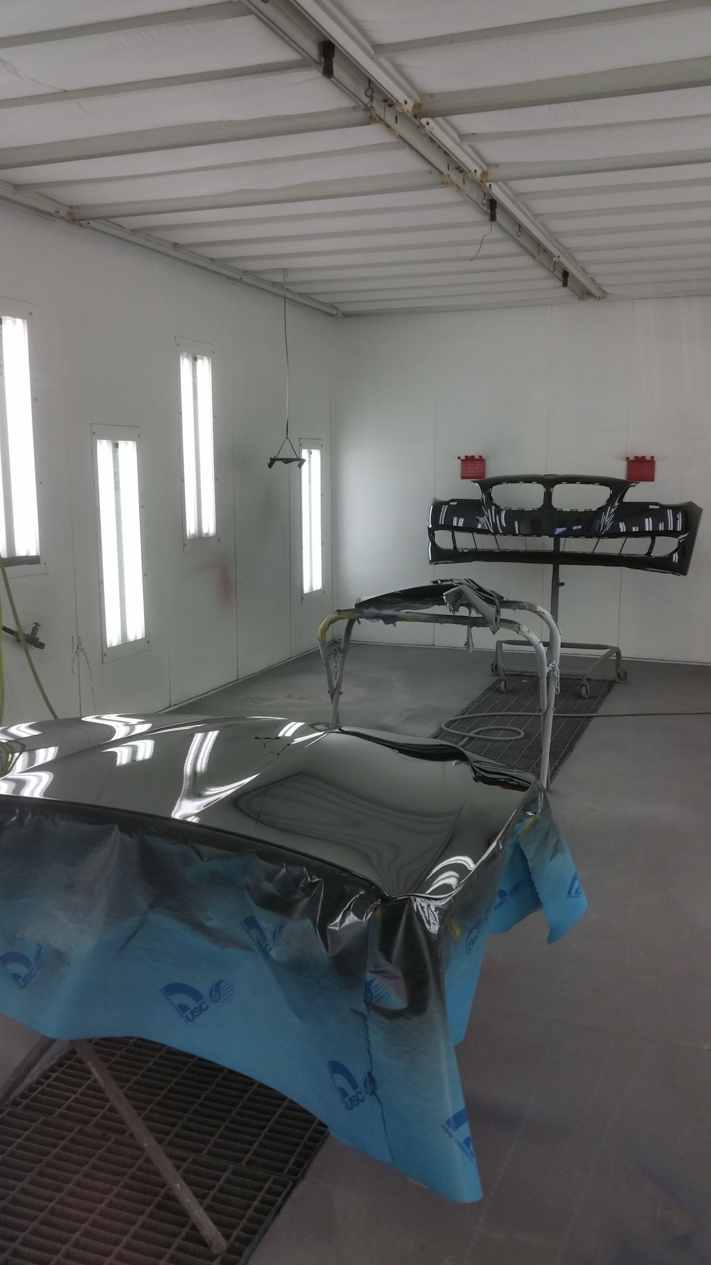 A car paint booth with car parts, covered in plastic, ready for paint.