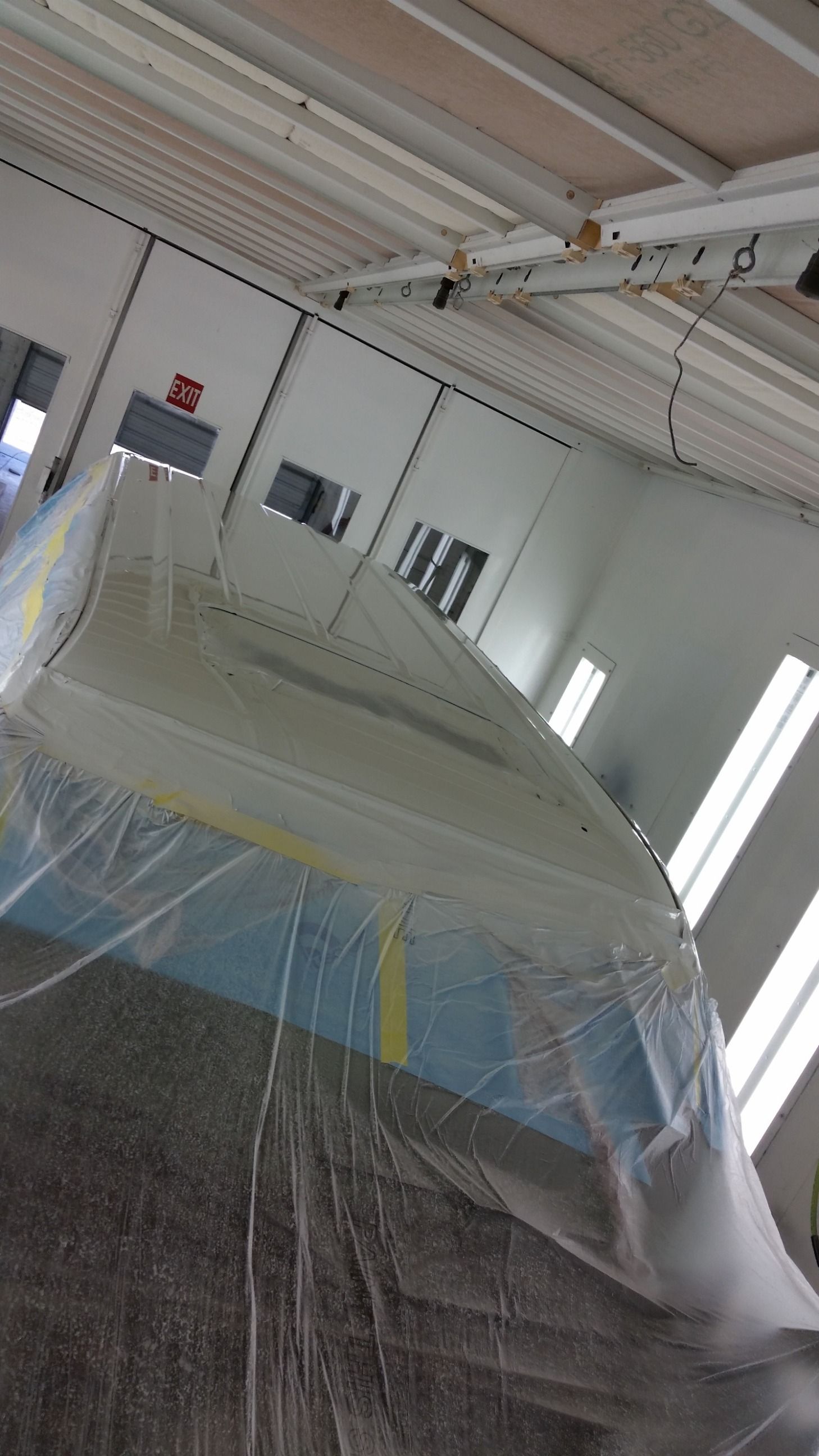A vehicle covered in plastic wrap inside a spray booth for painting.