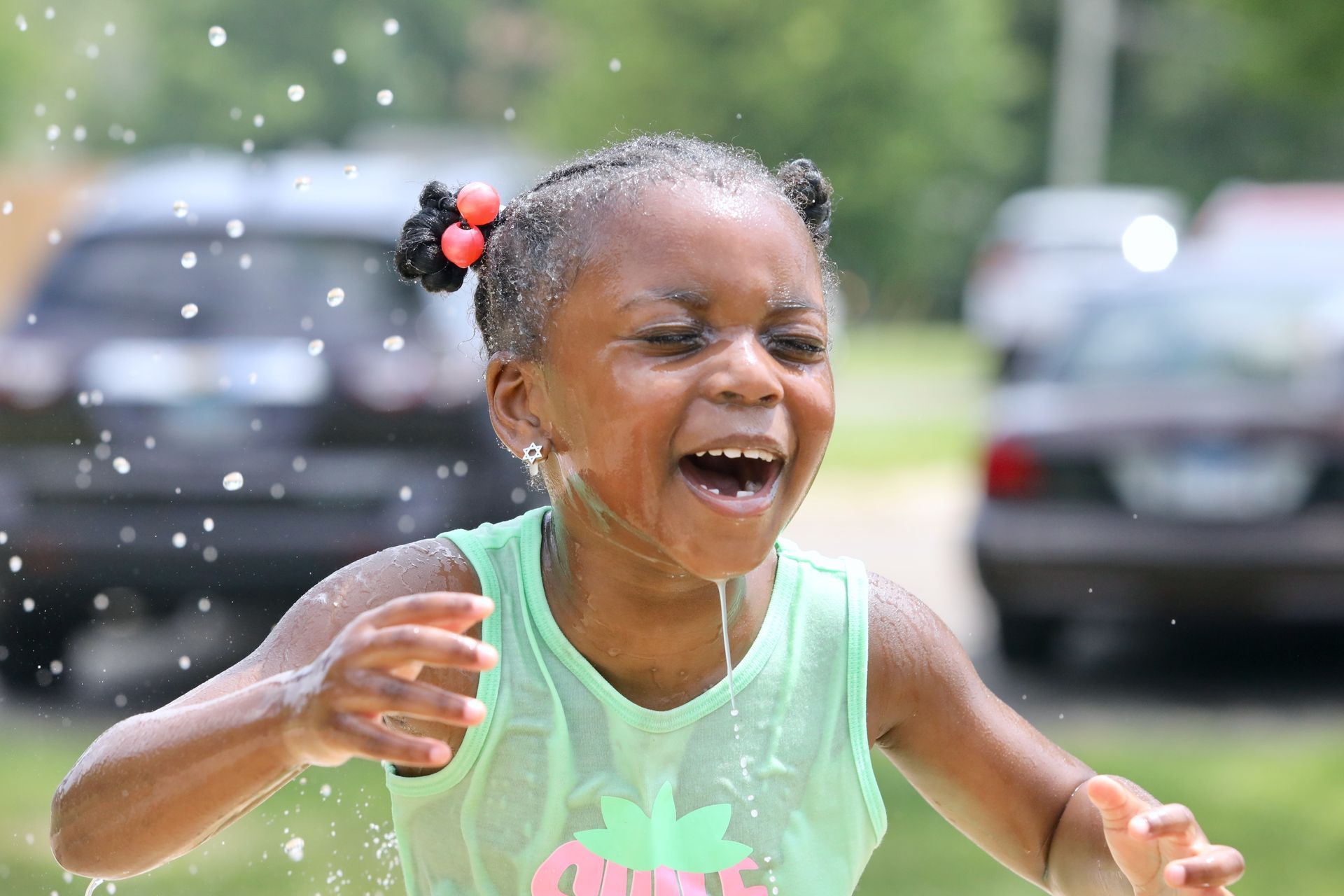 Young person smiling, getting splashed with water outdoors.