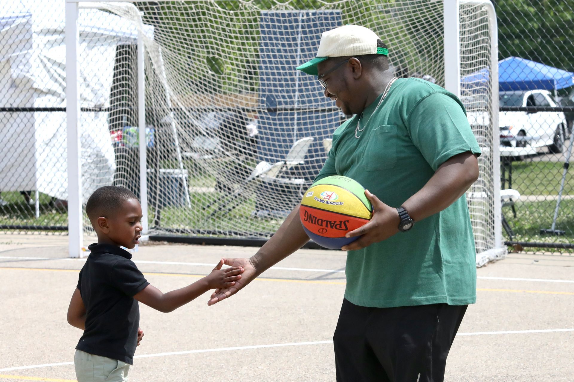 Man giving a basketball to a child outdoors on a court.