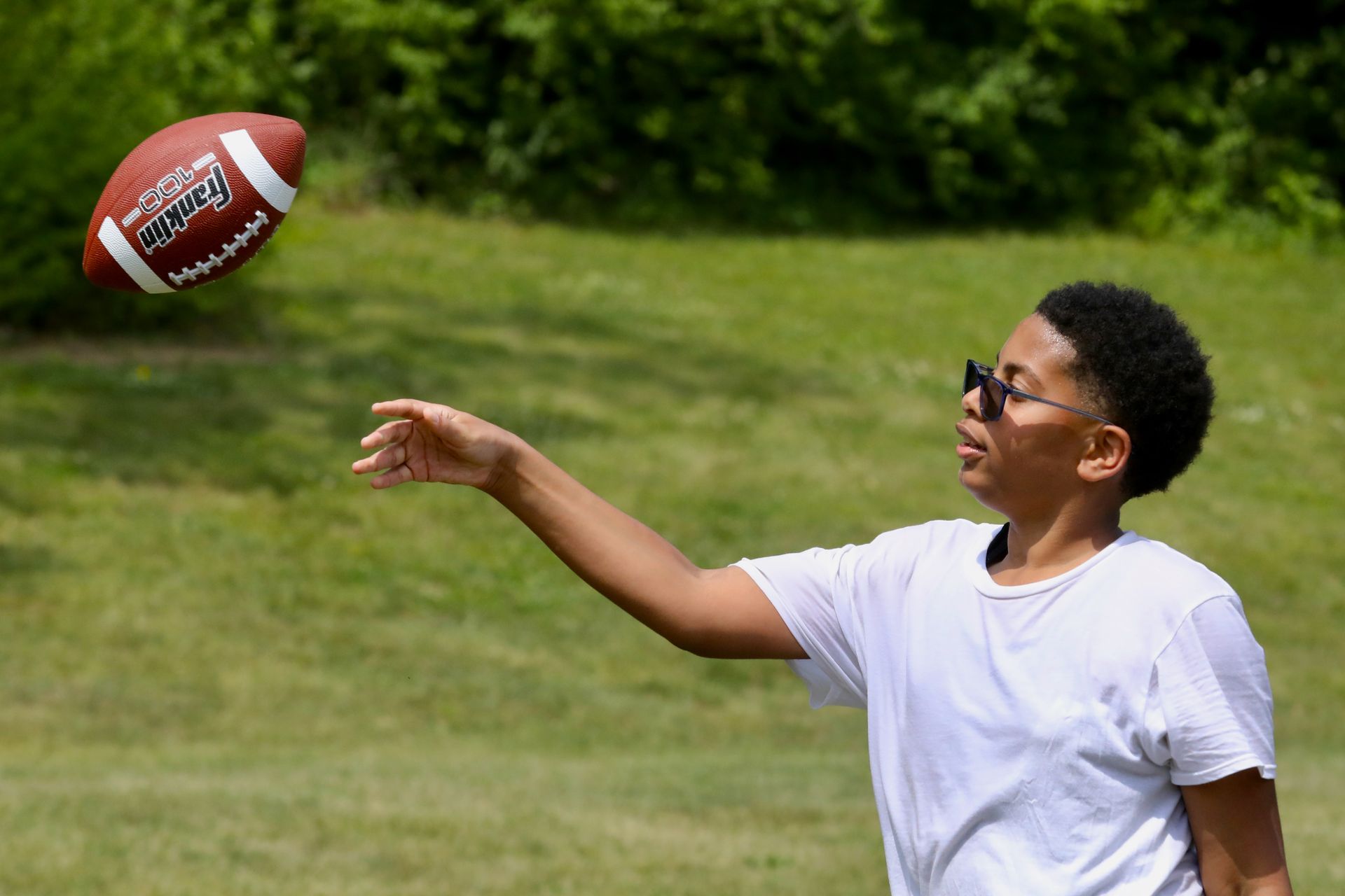 Person throwing a football in a sunny, grassy outdoor area.