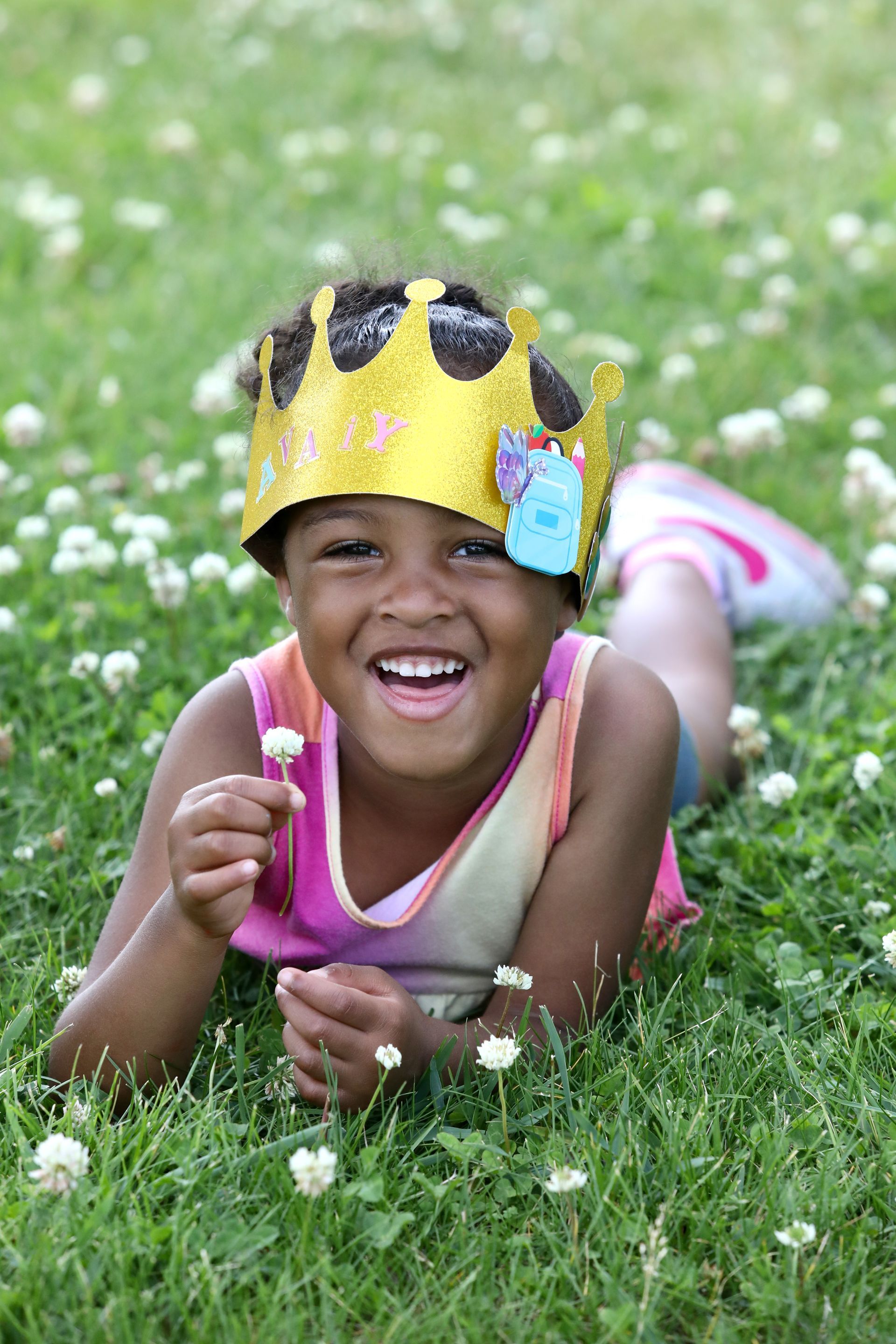 Smiling child wearing a gold crown, lying in a field of clover.