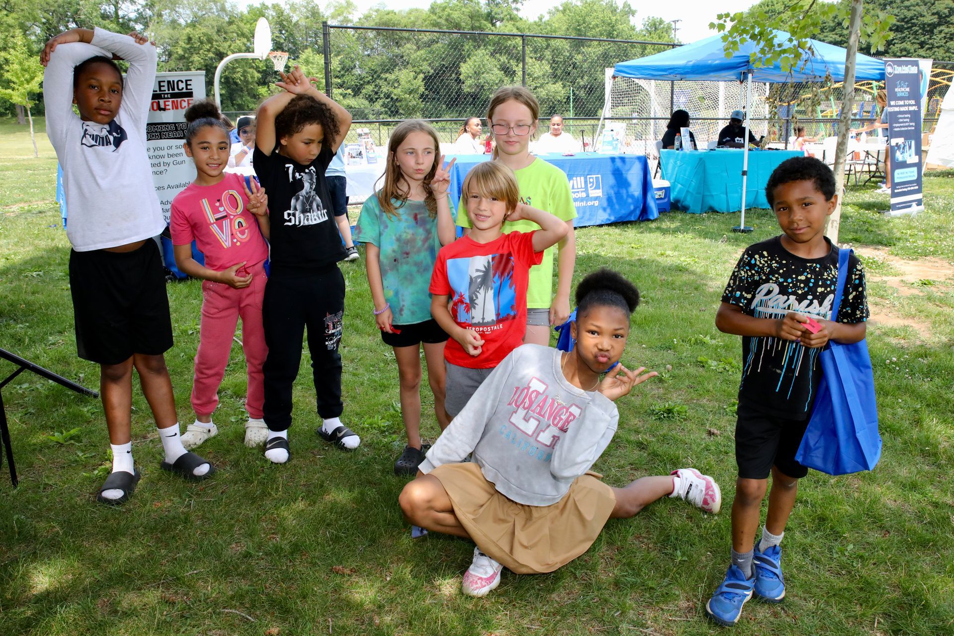 Group of children pose on grass in front of a blue tent, some smiling.