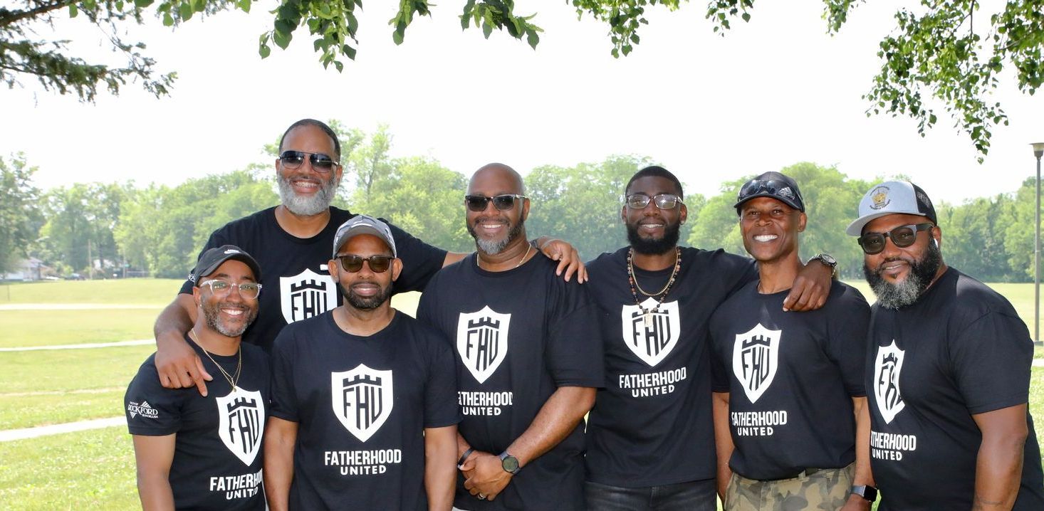 Group of people in black shirts with a shield logo, posing outdoors, smiling.