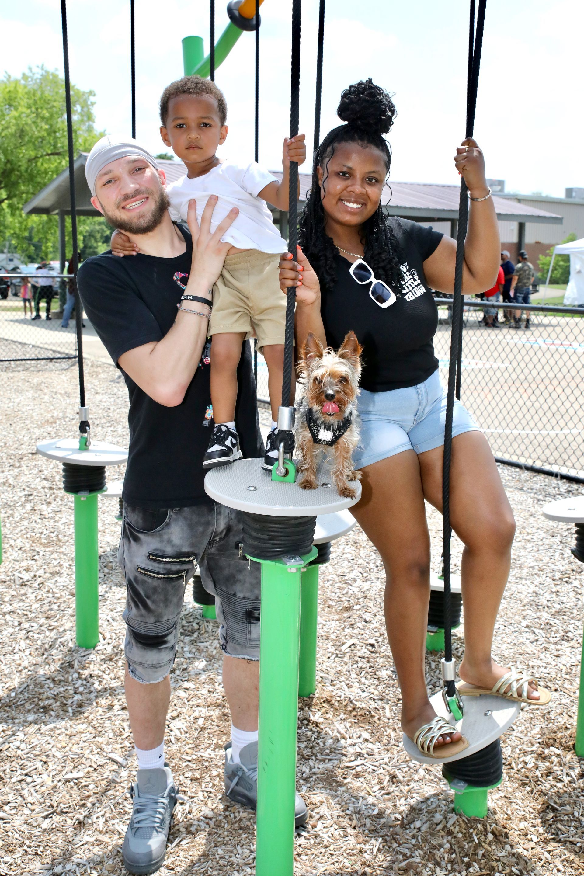 Family of four on playground equipment. Smiling man, boy, woman, small dog pose on platforms.