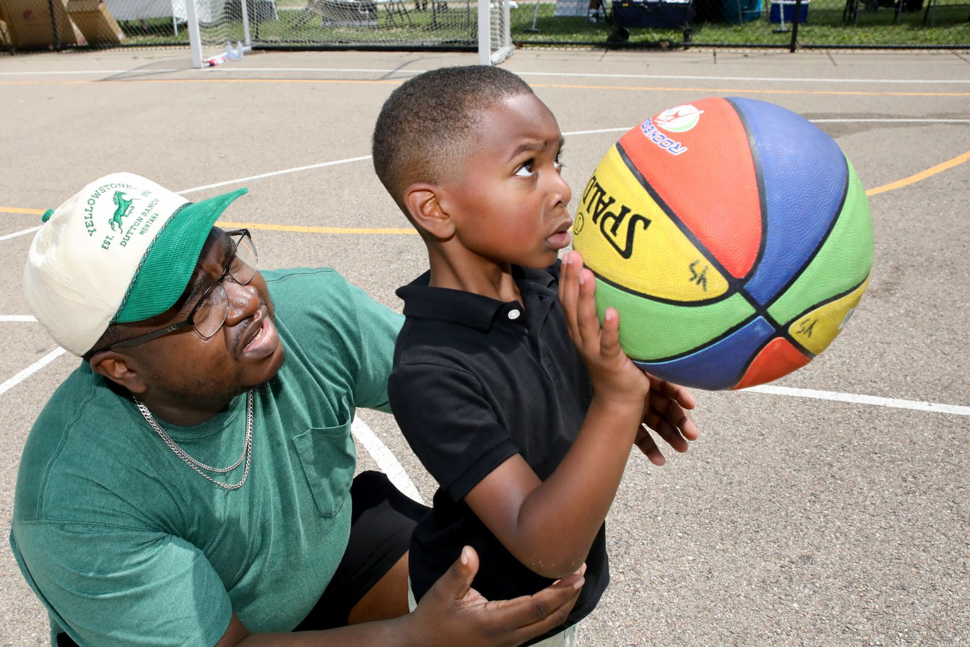 Man helping a child hold a colorful basketball on a court.