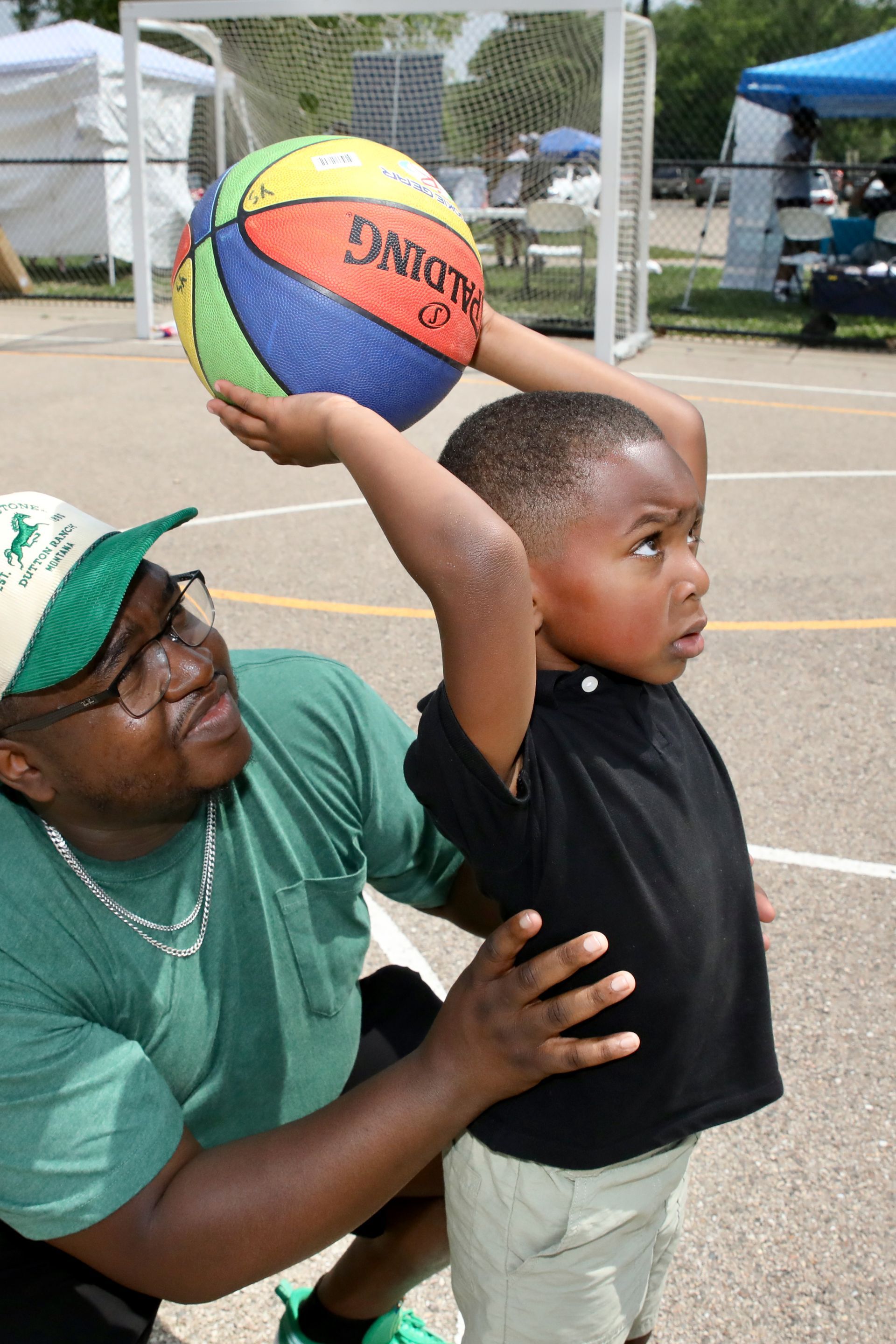 Man helping a child hold up a basketball on a court.