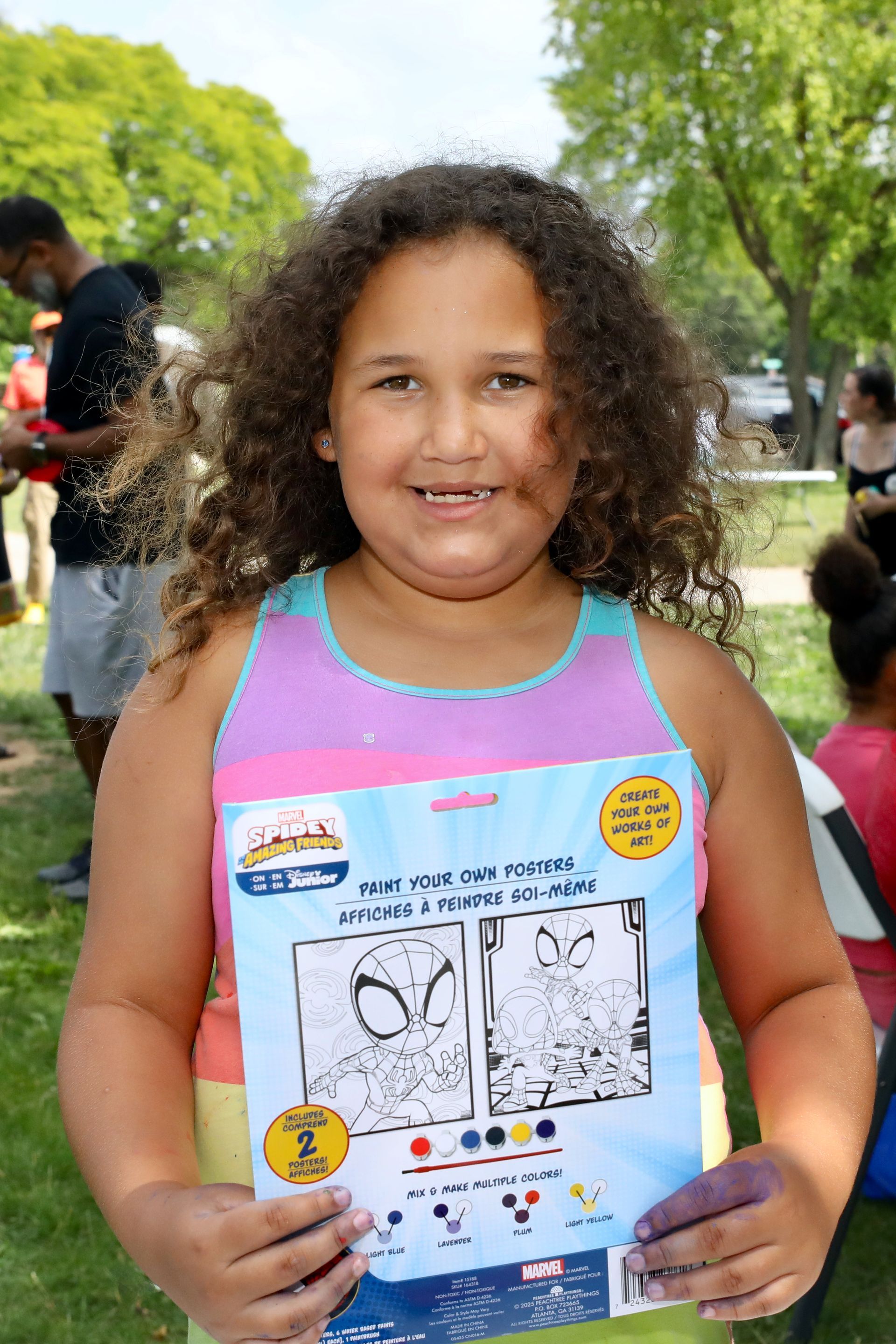 Girl holding a Spider-Man coloring kit, smiling outdoors.