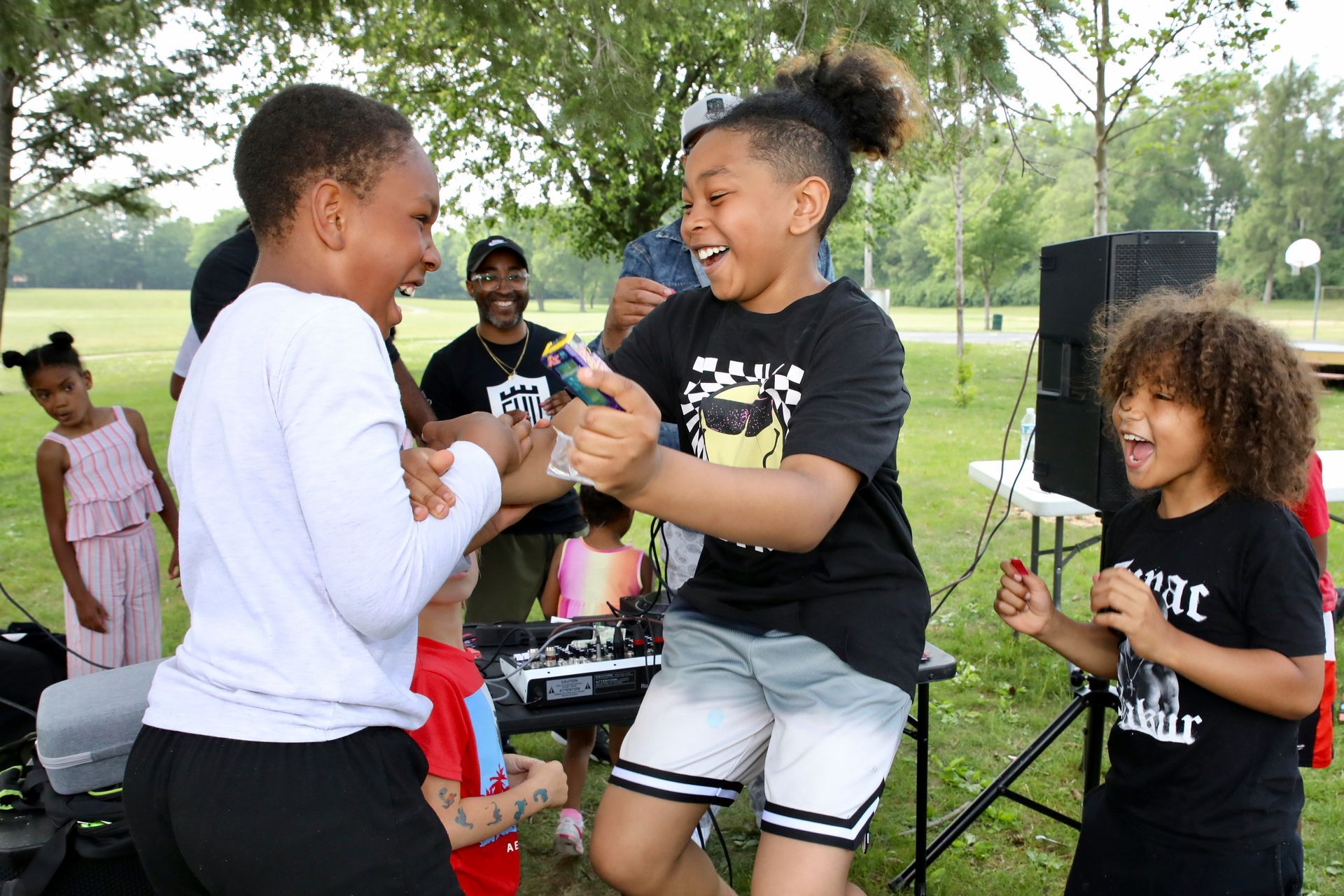 Children dancing and celebrating at an outdoor event with a DJ and a trophy.