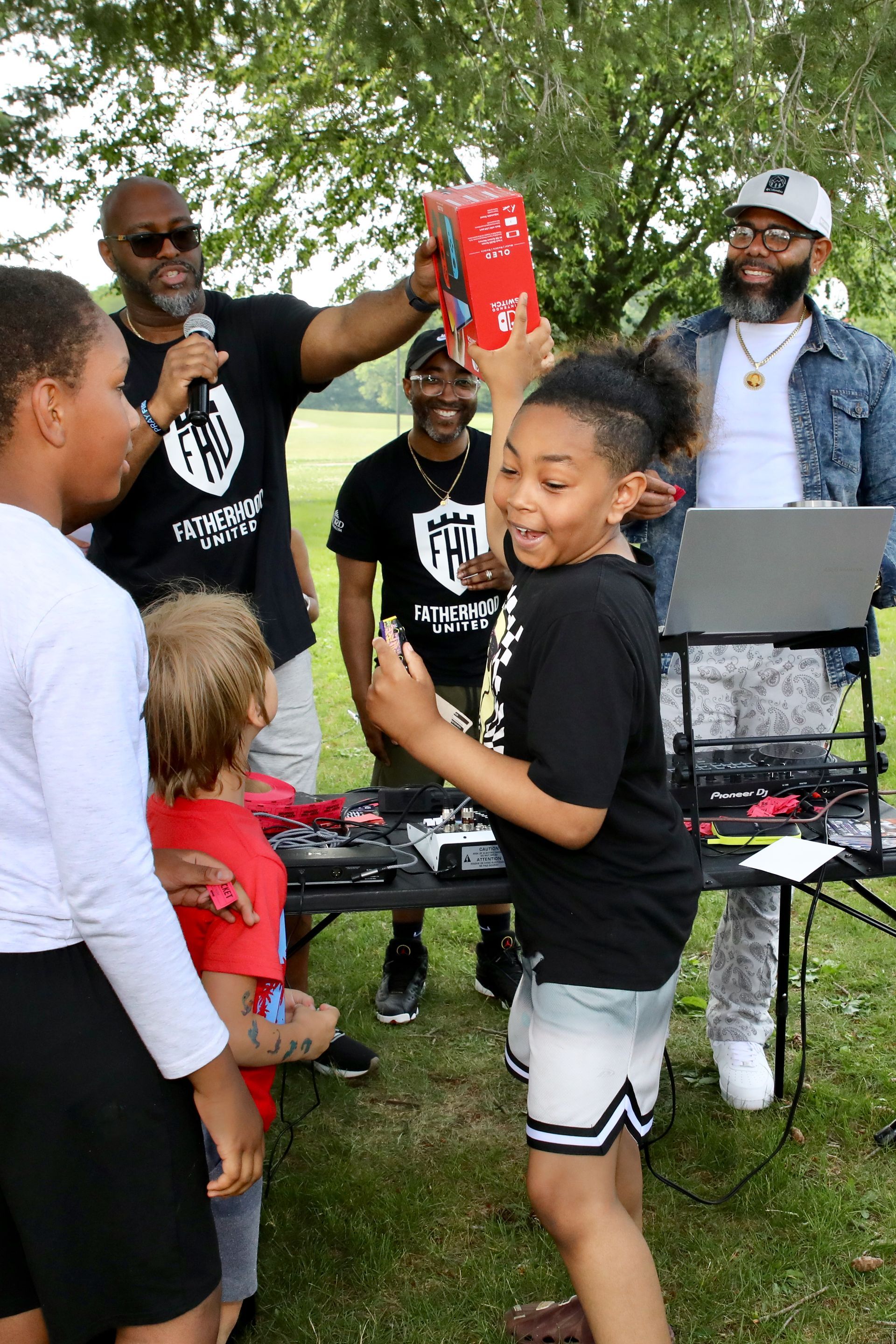 Group of people at an outdoor event. A child excitedly holds a prize while others look on.