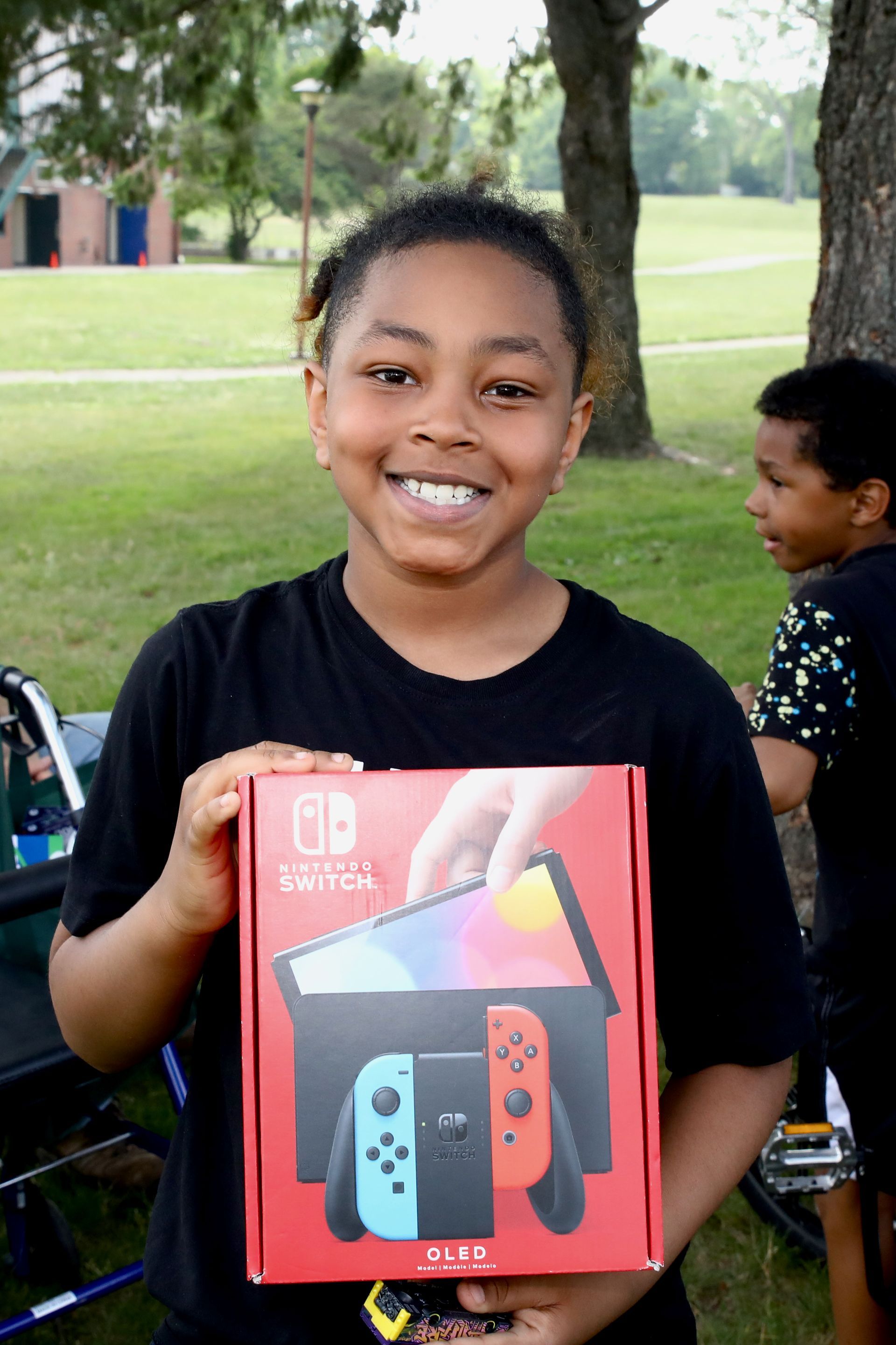 Young person smiling, holding a Nintendo Switch box outside.