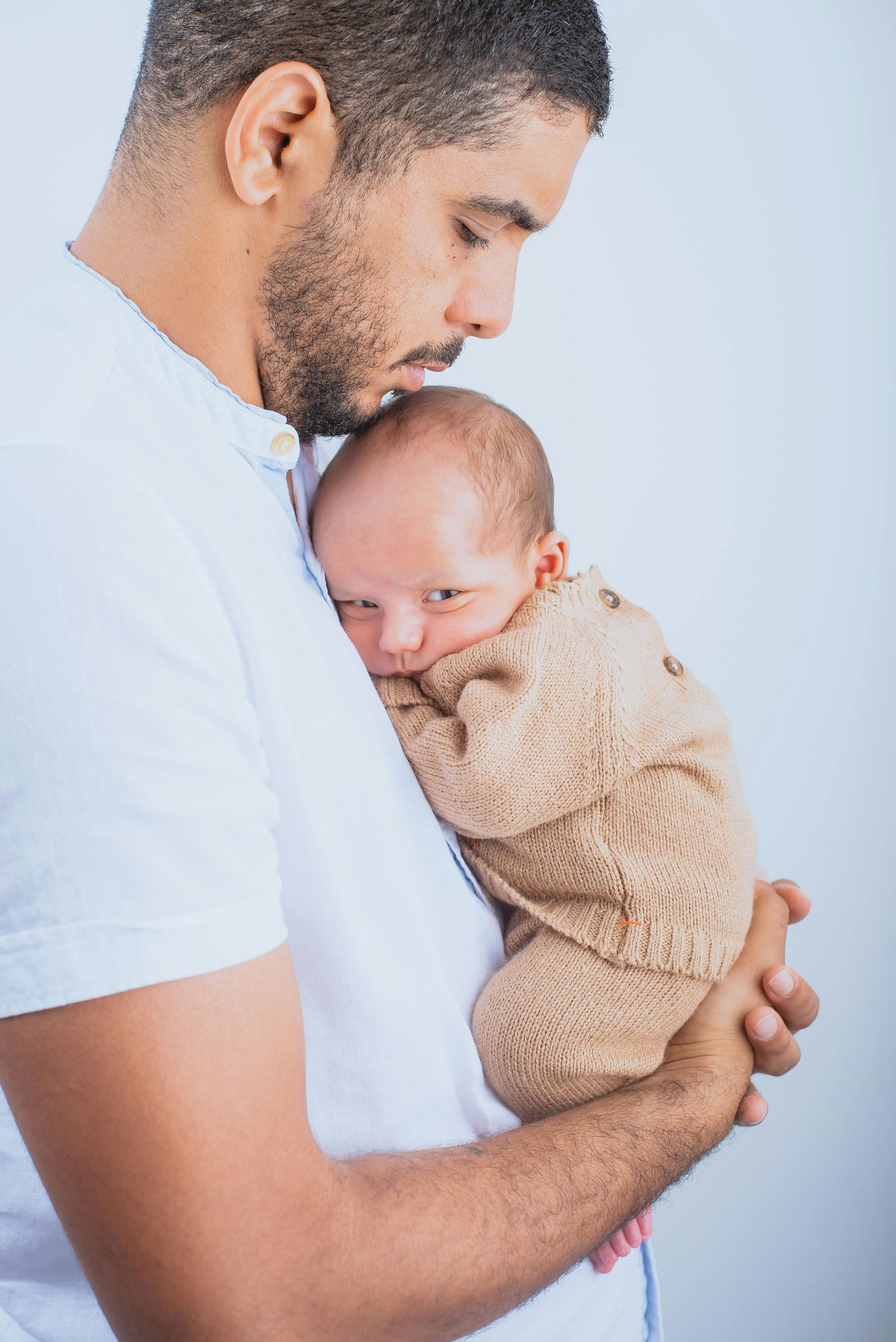 Man holding a newborn baby close. The baby is wearing a beige knit outfit.