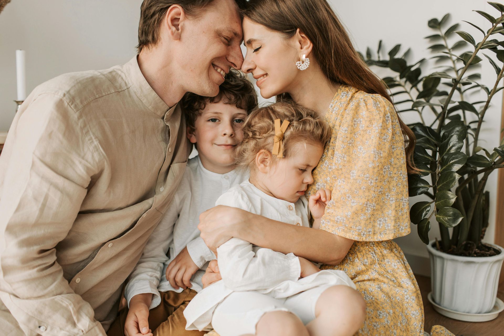 Family of four smiling, embracing; parents touching foreheads with children close by.